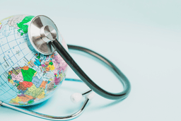 A stethoscope placed on a colorful globe, symbolizing global health care and the importance of worldwide medical attention on a light blue background.