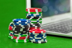 Stacks of multicolored poker chips are placed on a green surface next to a laptop keyboard, suggesting online gambling or virtual casino gaming.